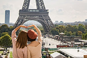 Two women making a heart with their arms in front of the Eiffel Tower